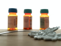Bild zeigt 3 Medikamentendosen im Hintergrund und einen Löffel mit Tabletten im Vordergrund
